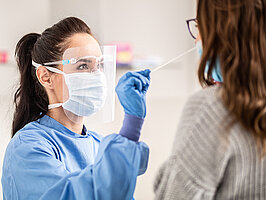 Female medical staff worker wearing protective equipment takes sample from nose of a patient to antigen test for coronavirus.