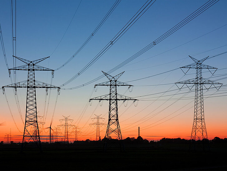 Strommasten bei Sonnenuntergang mit Windrädern am Horizont