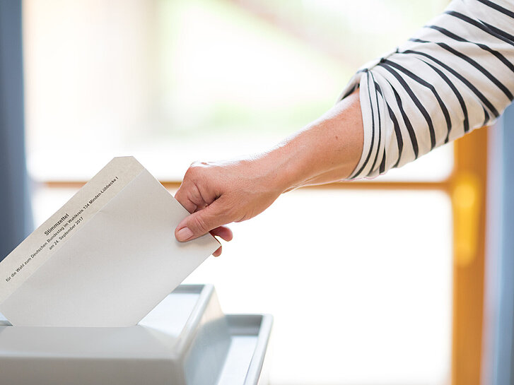 Stimmzettel wird in eine Wahlurne geworfen