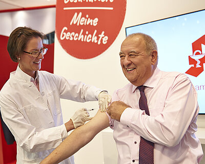 Dr. Theda Napp impft Fritz Becker am ABDA-Stand auf der expopharm in Düsseldorf (Foto: ABDA/Hinz)