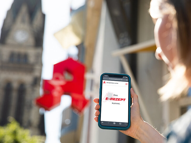 Frau mit Smartphone vor einer Apotheke